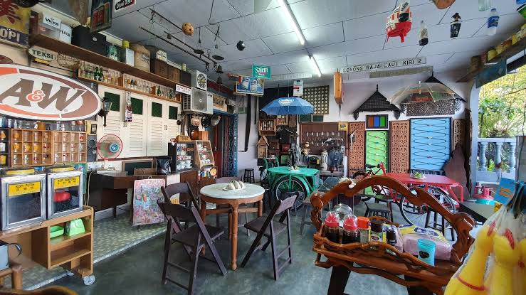 Ruang dalam Warung Pak Ali: meja marmar bulat, kerusi kayu, papan tanda lama dan hiasan antik di dinding